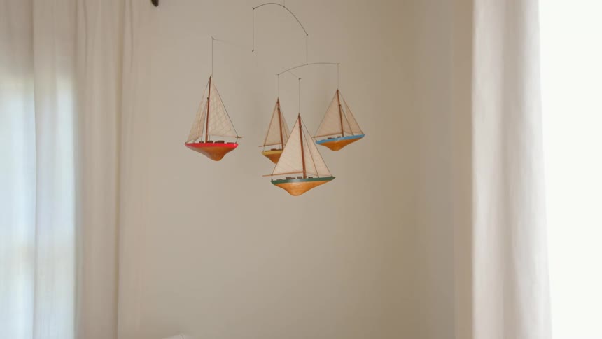A sailboat themed mobile hangs in a softly lit nursery corner