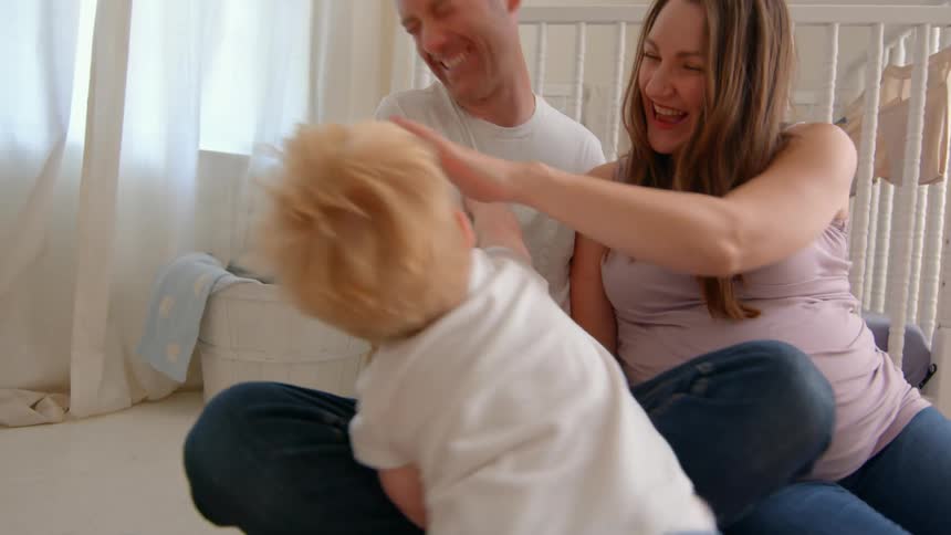 Young family laughs together on nursery floor with toddler