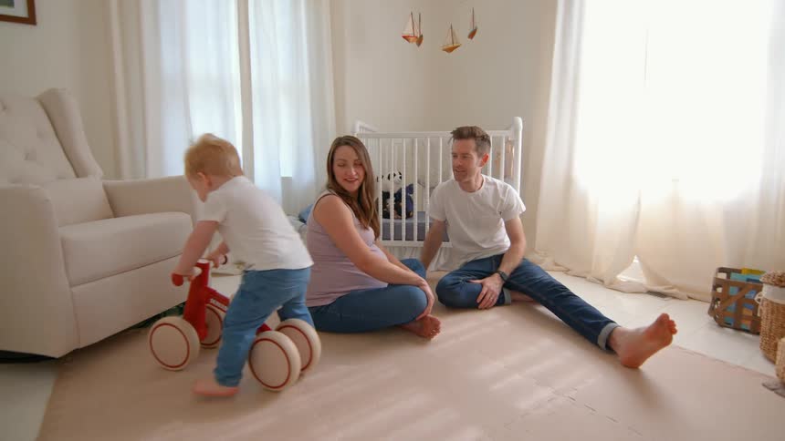 Father and pregnant mother sitting in the room with a child playing with a toy