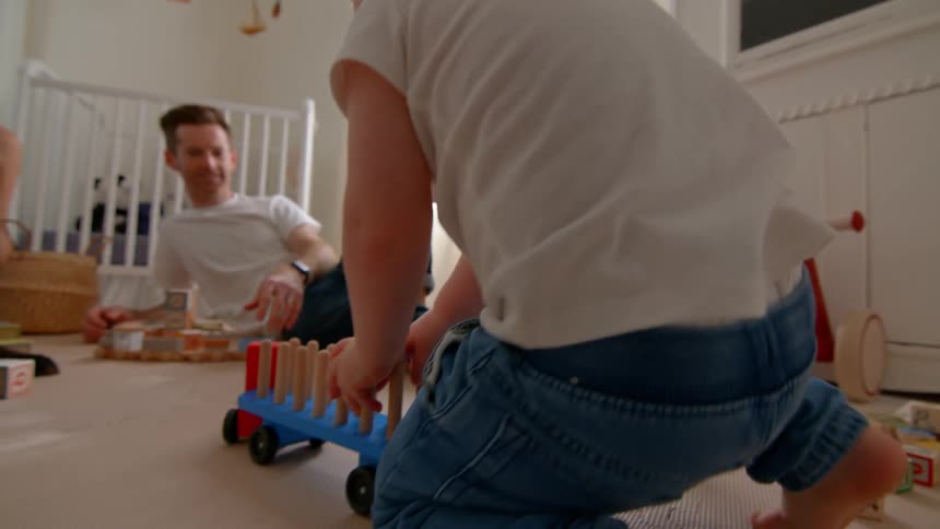 The dog watches as the boy pushes his toy truck