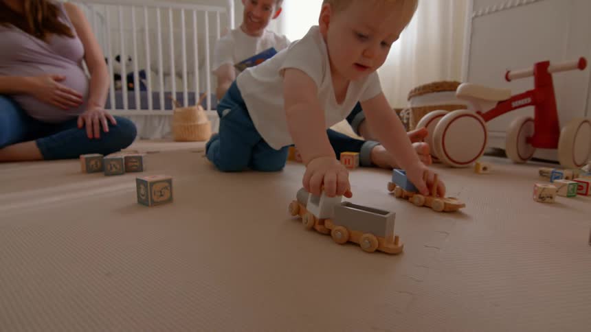 Toddler plays with toy trains as family watches
