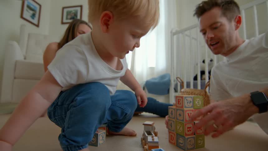 Toddler plays with blocks as parents join on nursery floor