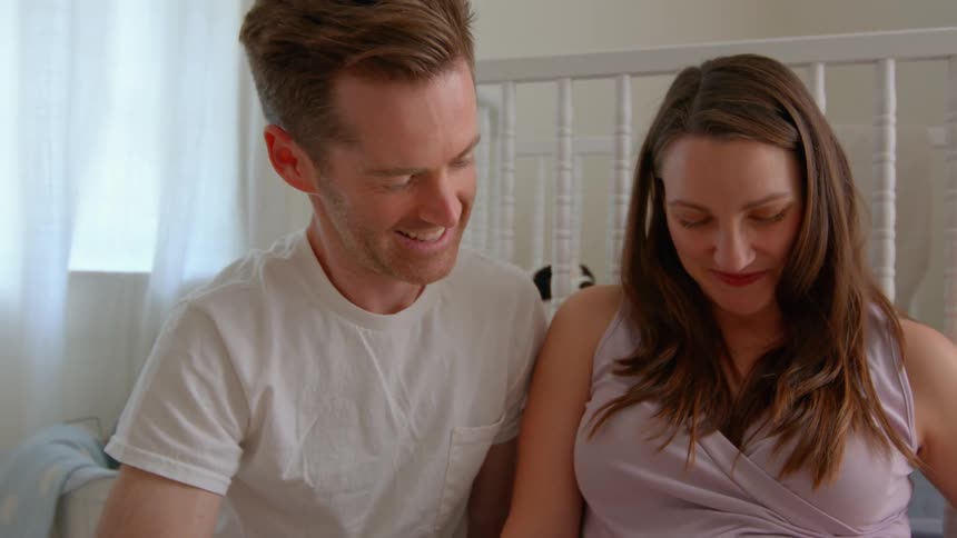 Man hugging his pregnant wife in a room with a crib