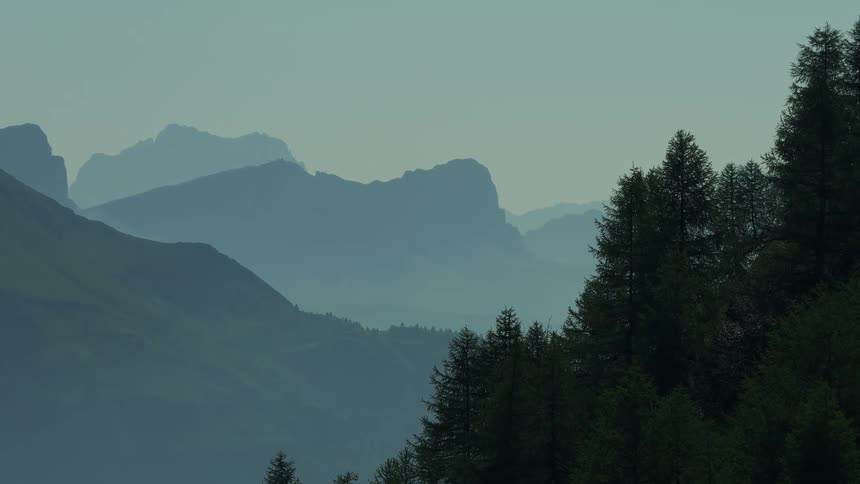 Layered mountain ranges stretch toward the horizon under a clear sky with a dense forest of tall trees covering the foreground