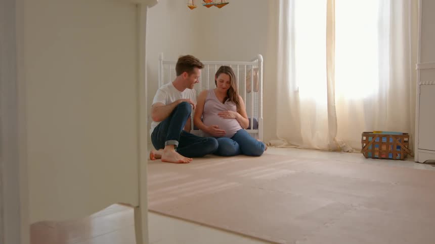 A man walks over and sits with his wife by the crib