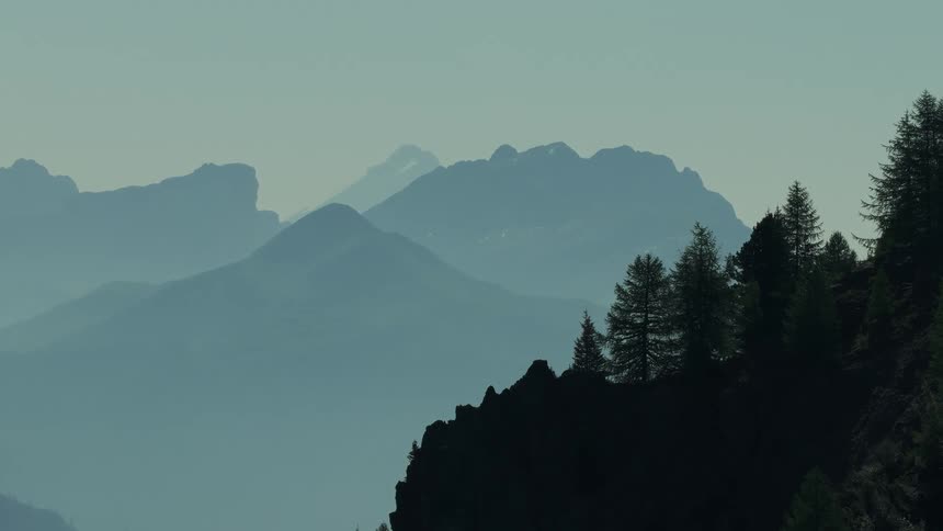 Silhouetted pines line a cliff with hazy mountains in the distance
