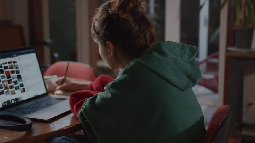 Woman writing on a paper with a laptop open in front of her