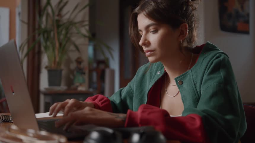 Woman wearing a green jacket sitting behind a coffee table typing on her laptop