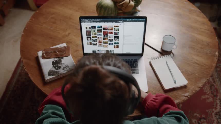 A person wearing headphones works on a laptop at a round wooden table