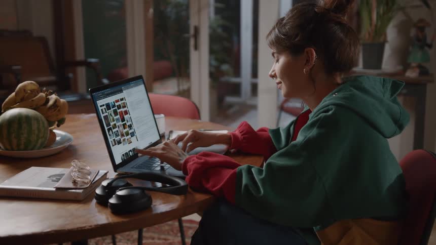 A woman types on her computer while sitting in her dining area