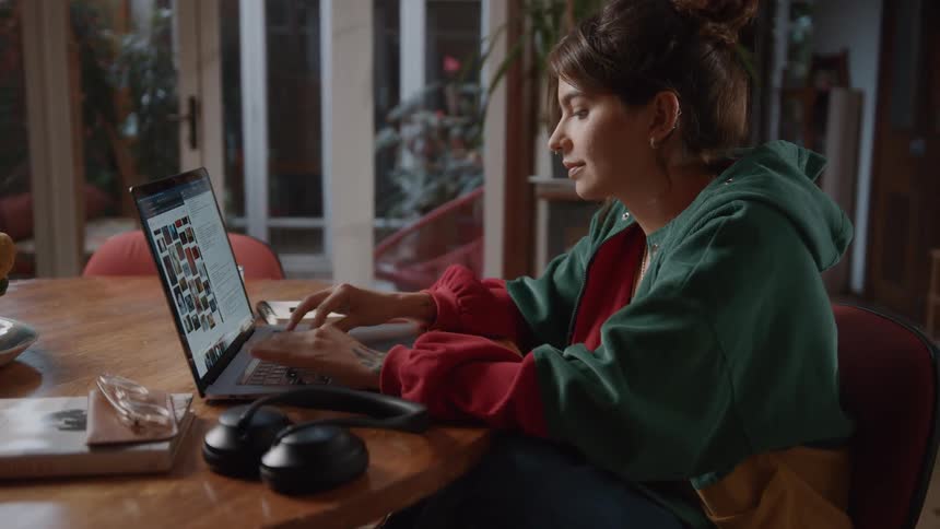 A woman is working on a laptop at a wooden table in a cozy indoor setting