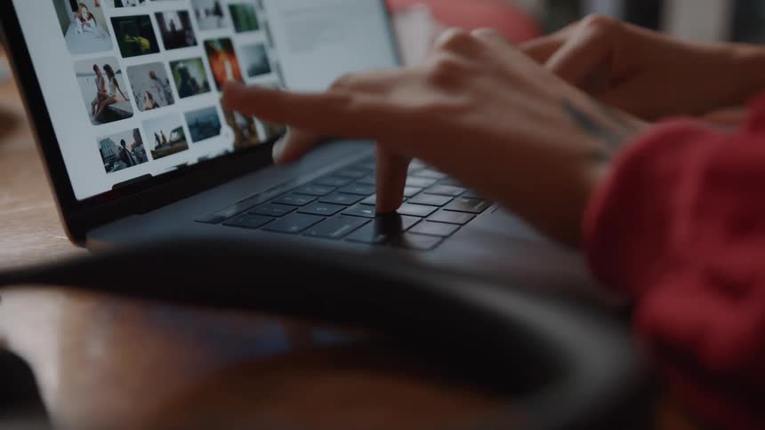 Close up of a persons hands as they type on a laptop computer on a tabletop