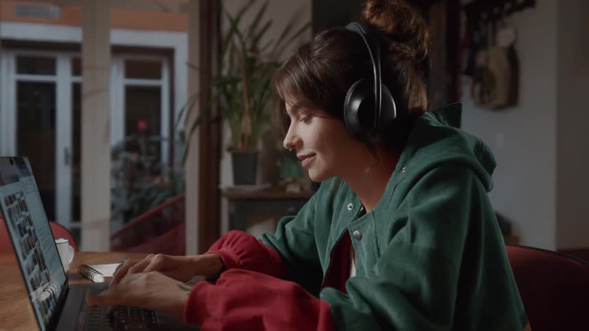 Woman with headphones sitting at a table interacting with a laptop