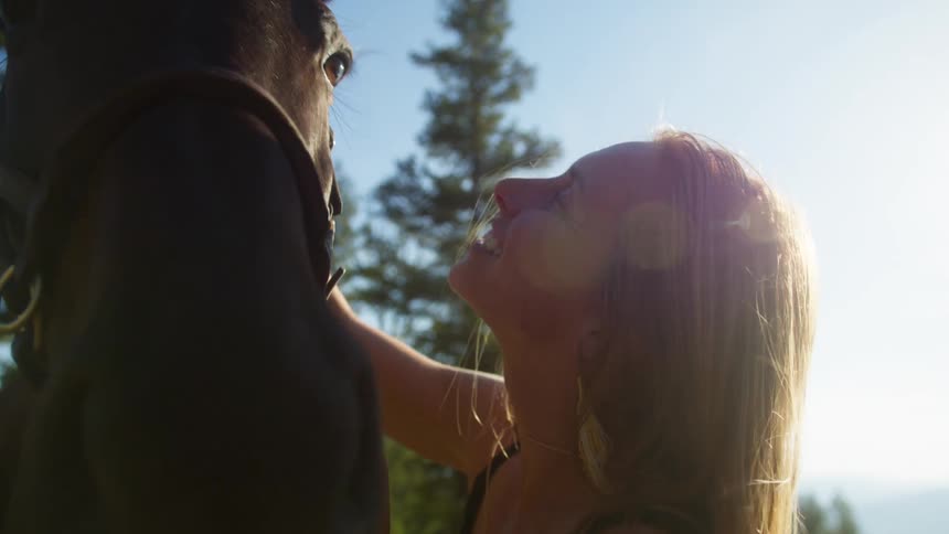 Close up of a young woman playfully rubbing her horse while standing outdoors during daytime