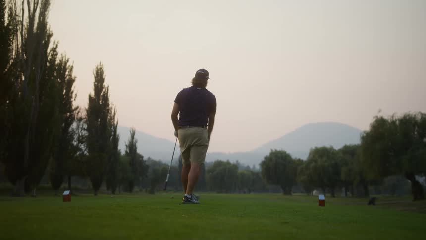 A man prepares to swing a golf club on a peaceful course at dusk