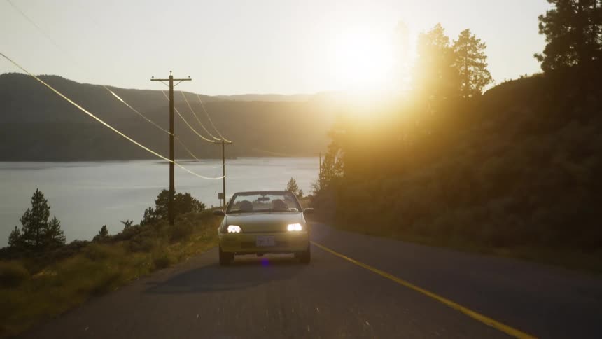 The car is driving on a road by the lake