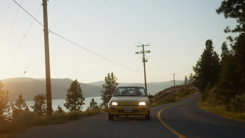 Acar drives along a winding road beside a lake during sunset