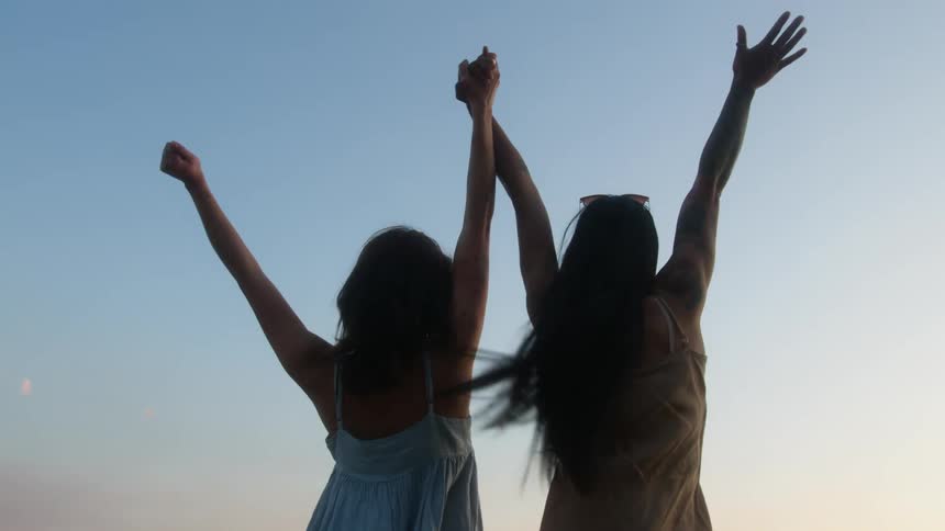 Two women raise their arms and cheer by the shore