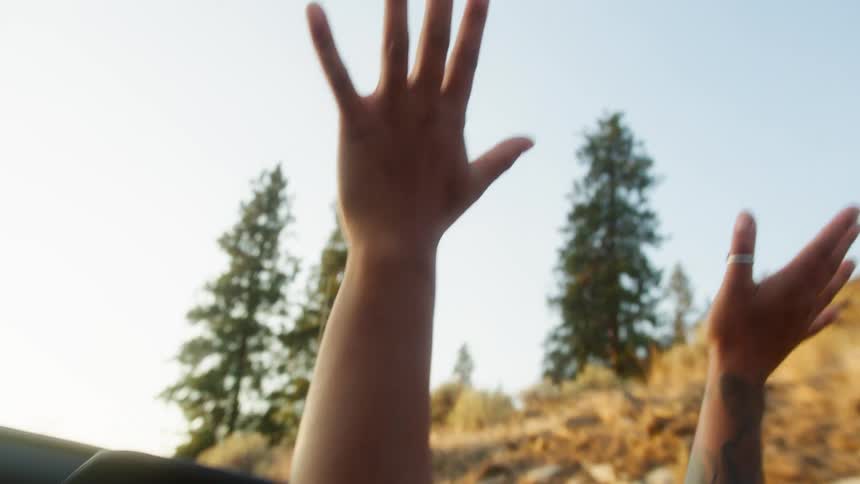 A woman smiles and raises her arms in the moving convertible