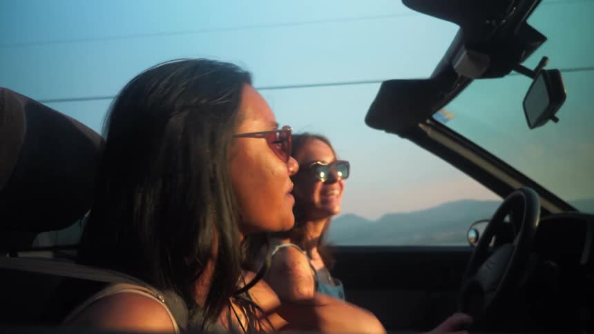 Two women inside a convertible car traveling and enjoying the vibe of the moment