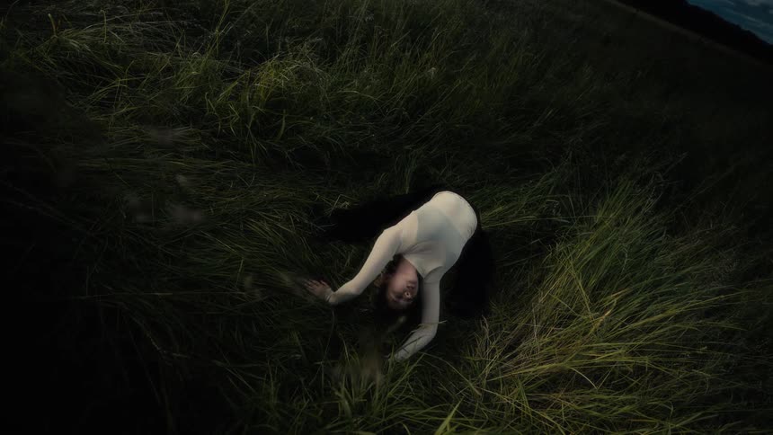 A woman moves gracefully through tall grass in a slow expressive dance