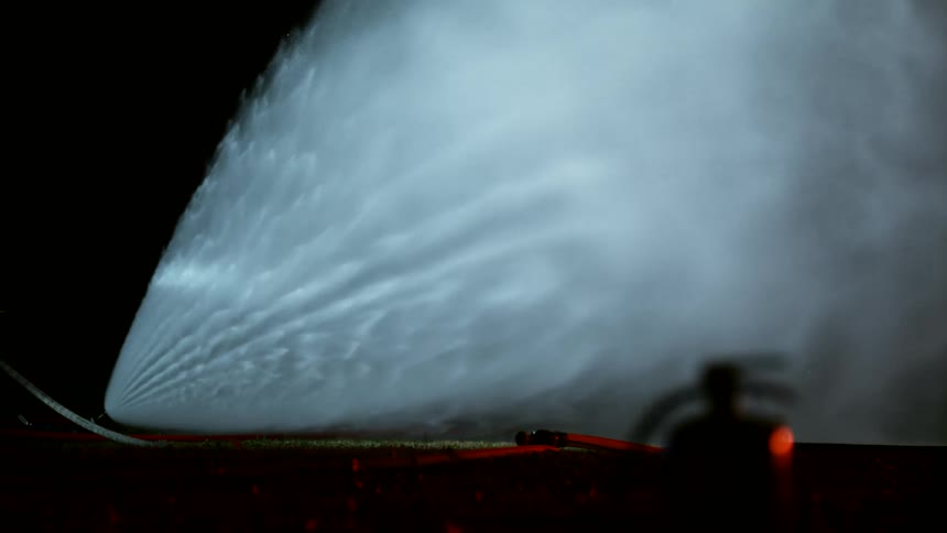 A hose sprays water on a fire at night
