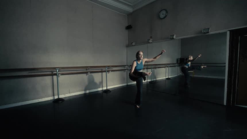 Woman dances in front of a mirror and ballet bar in a dark room