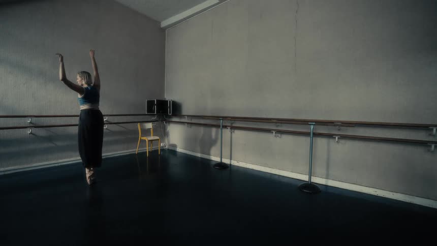 A young woman practices ballet in a dimly lit dance studio