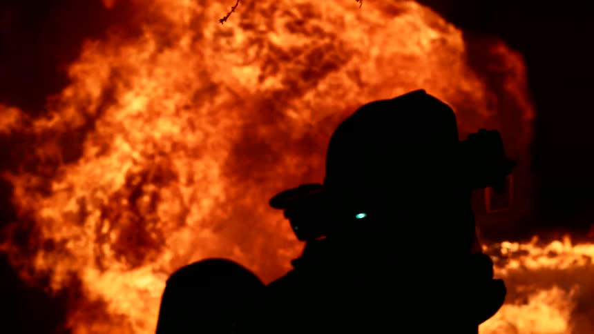 The firefighter sprays water on the fire at night