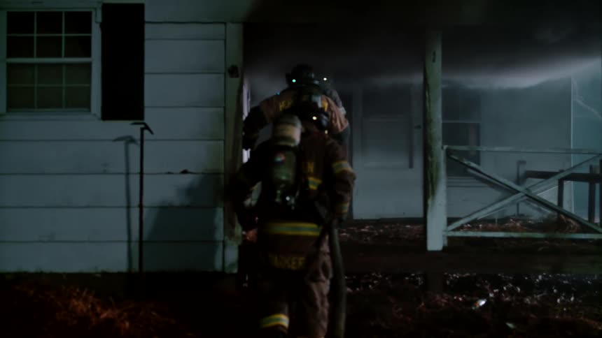 Firefighters with fire extinguisher in hose running towards a burning house at night