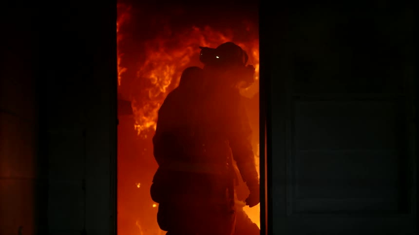 Firefighter entering a house at night that is on fire