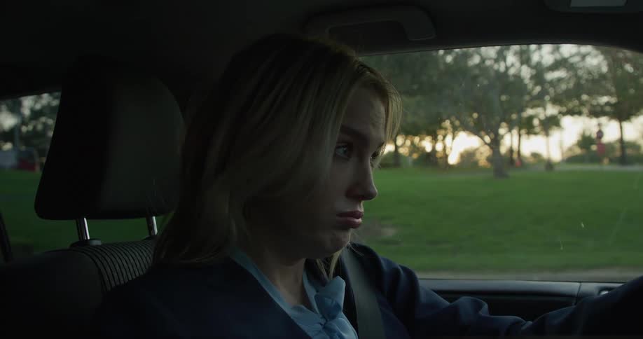 The woman smiles while looking in her back seat then drives
