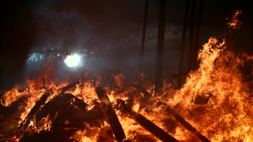 Flames rise from a blazing fire glowing in the darkness as a building burns to the ground and water flies through the air
