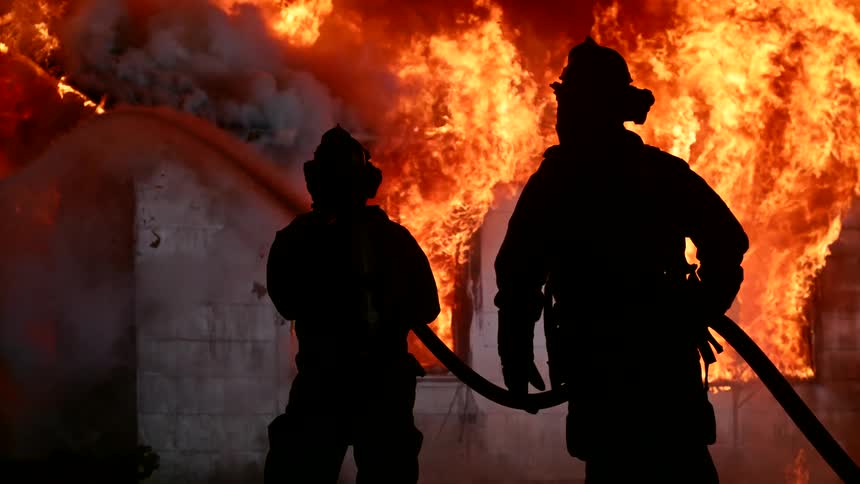 Blazing fire rages from a burning building as firefighters spray water on the fire