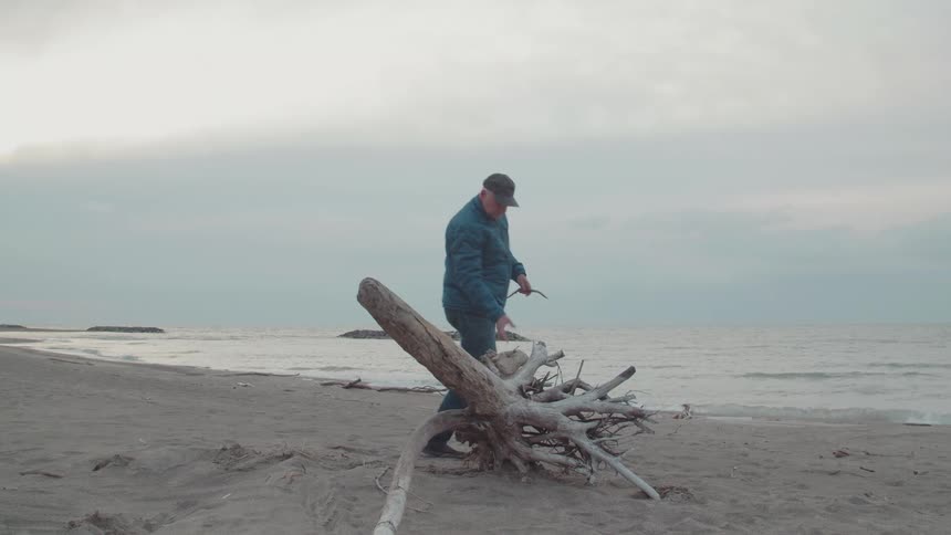 A man picks apart some driftwood on the beach