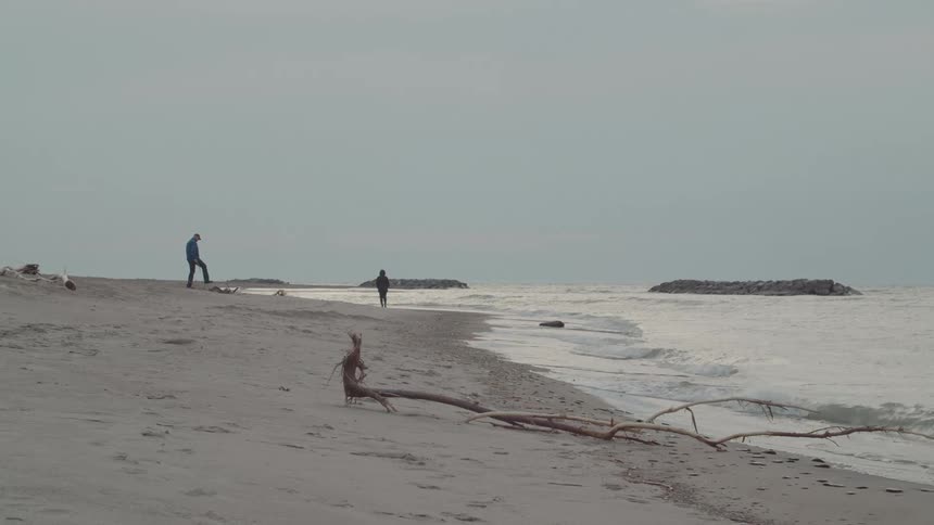 Two people walk along the shoreline at the beach as waves hit the shore around midday