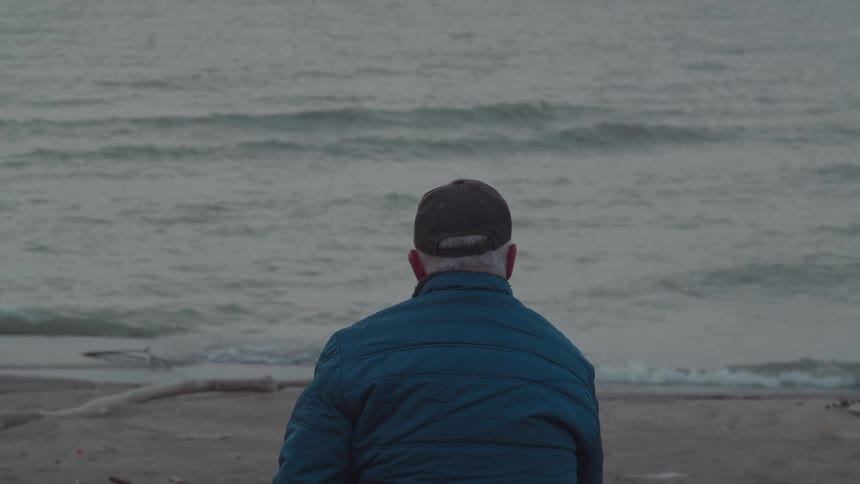 Man relaxing as he sits on the coast of a beach wearing a jacket