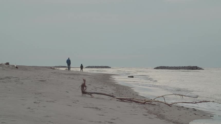 Two people walking on the sand at the beach on a cloudy day