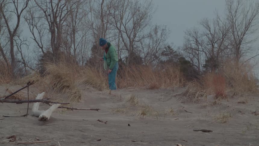 Two people on a winter day picking up twigs from a sandy environment
