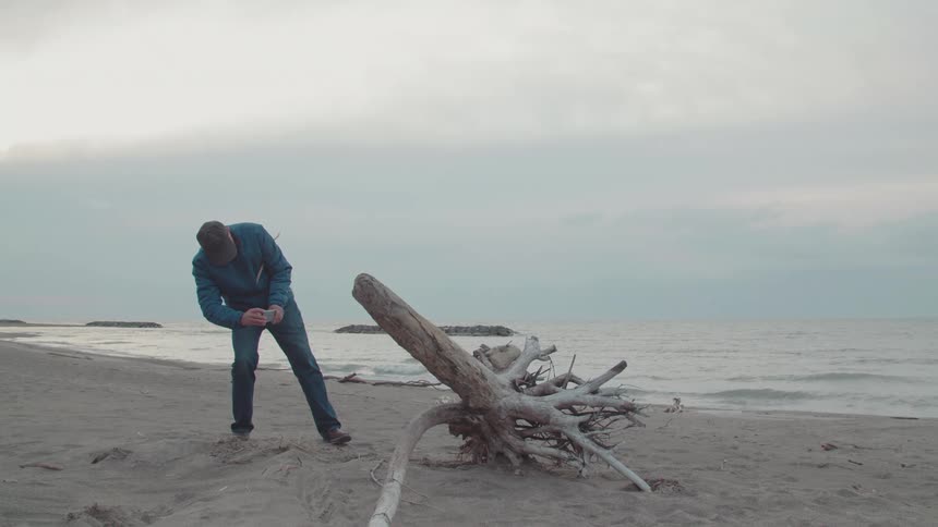 A man takes a picture of driftwood on the beach