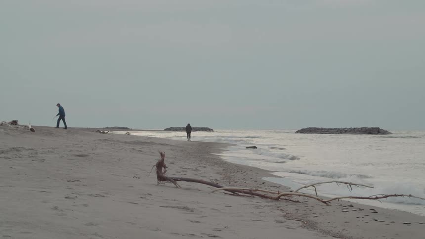 Two people walk along a quiet beach under an overcast sky