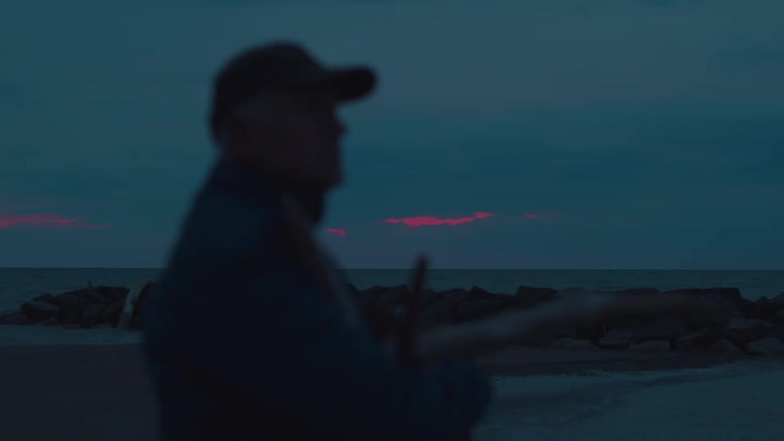 Silhouette of a man in a cap holding branches on a beach at dawn