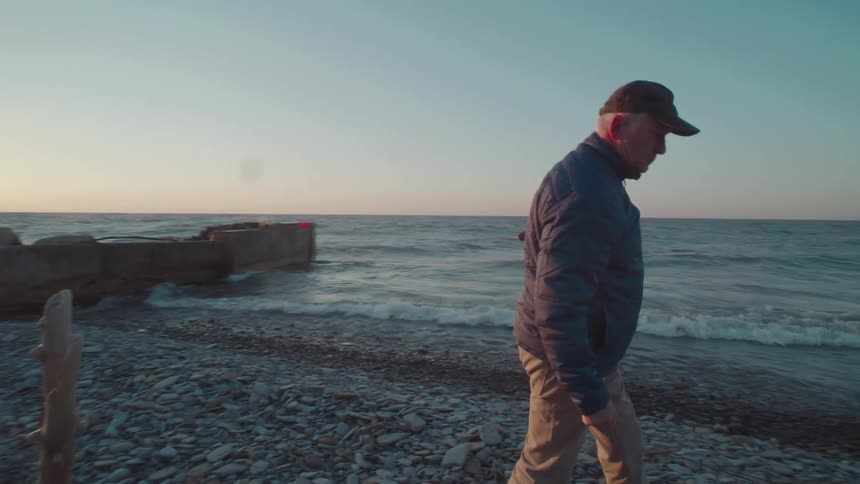 A man walks on a rocky shore near a pier and the ocean