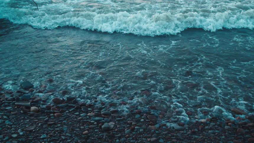Waves gently roll onto a rocky shoreline in the early blue light of dusk