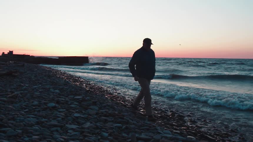 A man is walking down a beach at the edge of the water