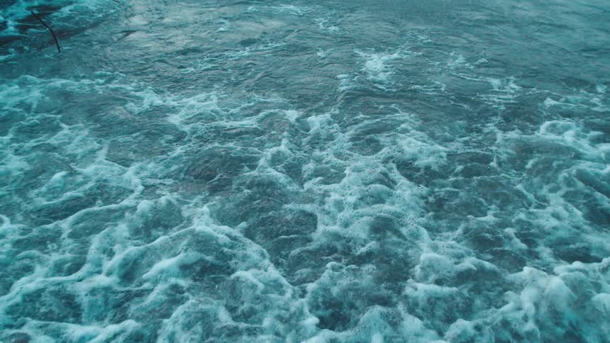 Waves crash onto a rocky shoreline in a top down coastal view
