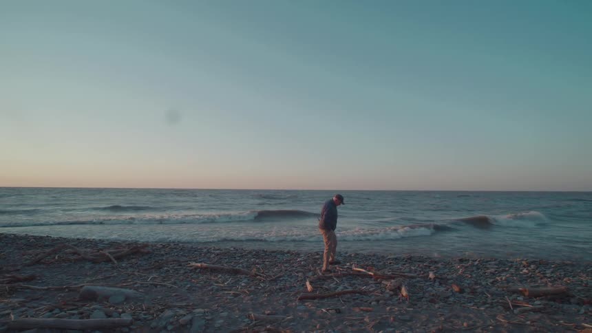 Man walking on the beach kicking driftwood as waves roll in to shore