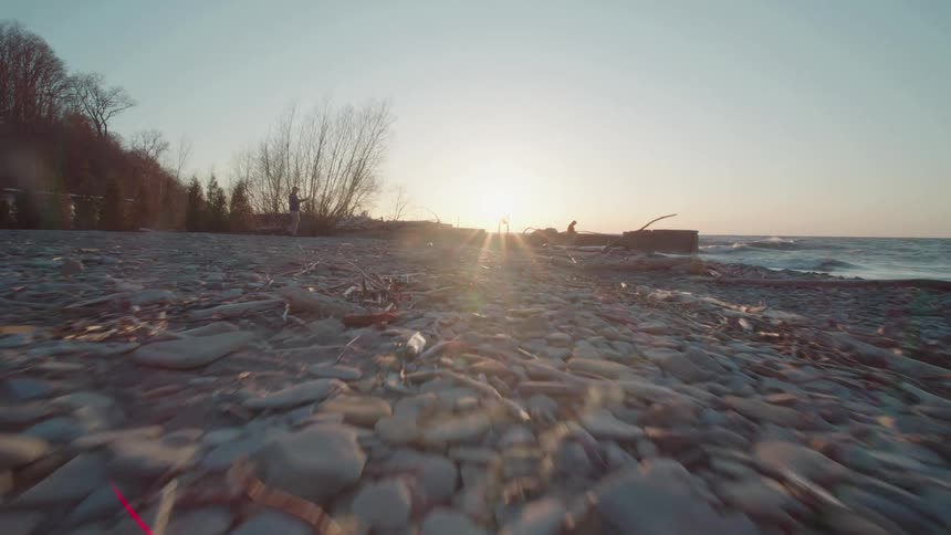 Two people walking among sand and rocks at dawn by the sea