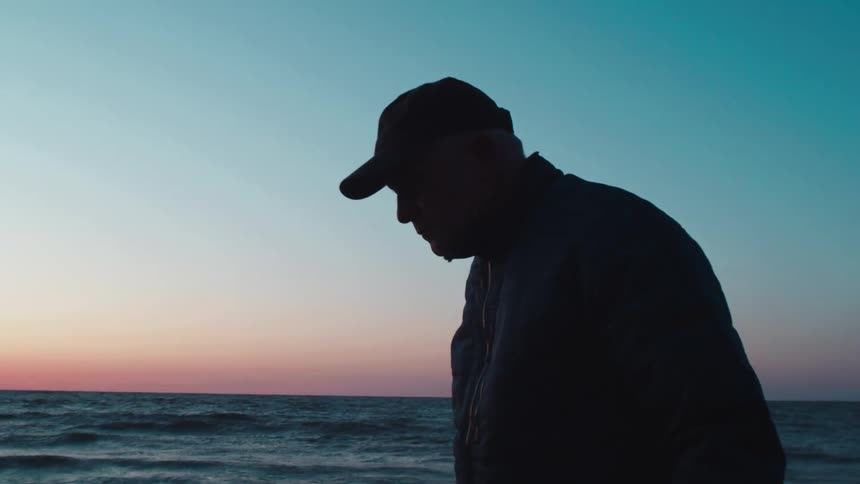 The man is walking by the water at sunrise