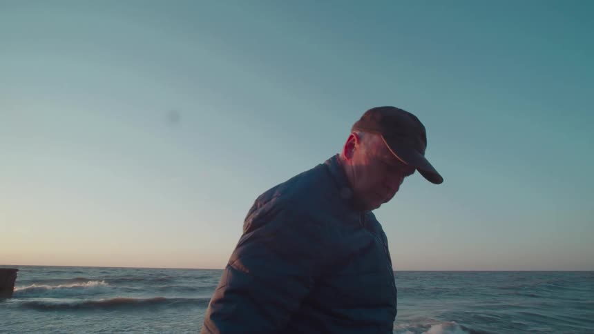 A man walks along the beach at sunset with sunlight flaring behind him